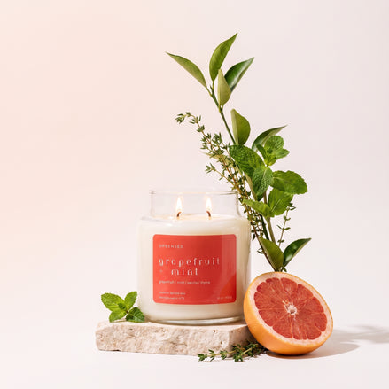Upsensed Grapefruit + Mint candle burning on a stone slab, styled with mint, thyme, citrus leaves, and a halved grapefruit.