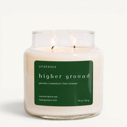 Upsensed Higher Ground 16 oz double-wick candle in a clear apothecary jar with a dark green label, petrichor, cedarwood, and fresh rainwater scent notes, on a plain white background.