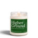 Higher Ground 8 oz soy candle by Upsensed, lit, in a clear glass jar with a forest green label listing petrichor, cedarwood, and fresh rainwater notes.