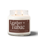 Leather + Tabac 18 oz double-wick soy candle by Upsensed, both wicks lit, in a clear glass jar with a brown label listing suede silk, leather, tobacco, and cherrywood notes.