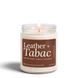 Leather + Tabac 8 oz soy candle by Upsensed, lit, in a clear glass jar with a brown label listing suede silk, leather, tobacco, and cherrywood notes.