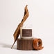 Upsensed Leather + Tabac candle burning on a round wooden pedestal, styled with a curled dried tobacco leaf and a coiled leather strap.