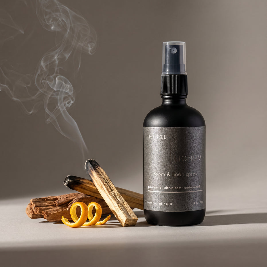 Upsensed Lignum Room and Linen Spray beside smoking palo santo sticks, cedarwood and citrus zest - woody home fragrance hand poured in Houston