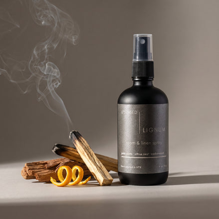 Upsensed Lignum Room and Linen Spray beside smoking palo santo sticks, cedarwood and citrus zest - woody home fragrance hand poured in Houston