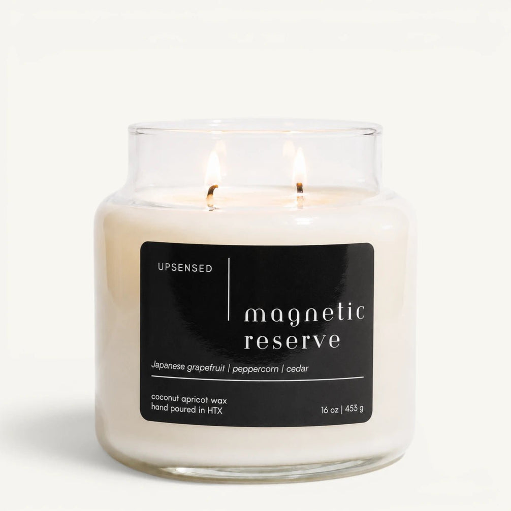 Upsensed Magnetic Reserve 16 oz double-wick candle in a clear apothecary jar with a black label, Japanese grapefruit, peppercorn, and cedar scent notes, on a plain white background.