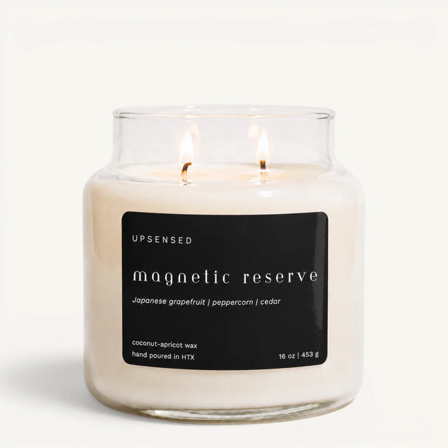 Upsensed Magnetic Reserve 16 oz double-wick candle in a clear apothecary jar with a black label, Japanese grapefruit, peppercorn, and cedar scent notes, on a plain white background.