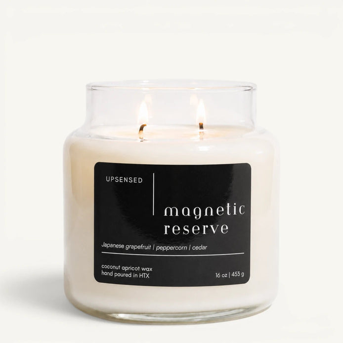 Upsensed Magnetic Reserve 16 oz double-wick candle in a clear apothecary jar with a black label, Japanese grapefruit, peppercorn, and cedar scent notes, on a plain white background.
