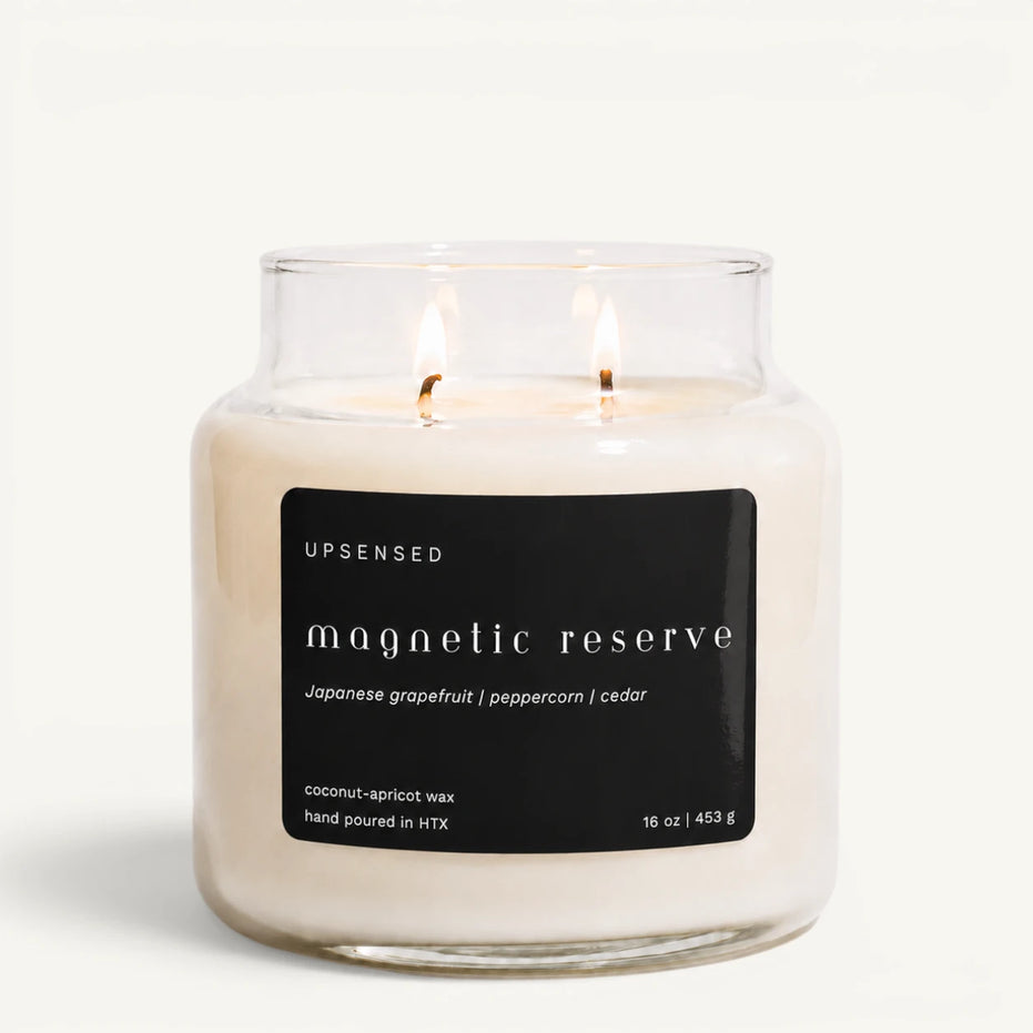 Upsensed Magnetic Reserve 16 oz double-wick candle in a clear apothecary jar with a black label, Japanese grapefruit, peppercorn, and cedar scent notes, on a plain white background.