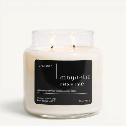 Upsensed Magnetic Reserve 16 oz double-wick candle in a clear apothecary jar with a black label, Japanese grapefruit, peppercorn, and cedar scent notes, on a plain white background.