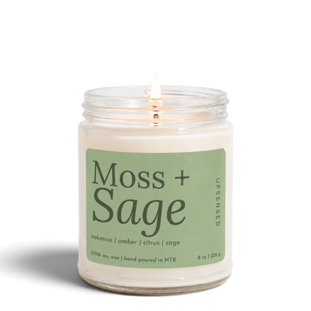 Upsensed Moss + Sage 8 oz soy candle, lit, in a clear glass jar with a sage green label listing oakmoss, amber, citrus, and sage