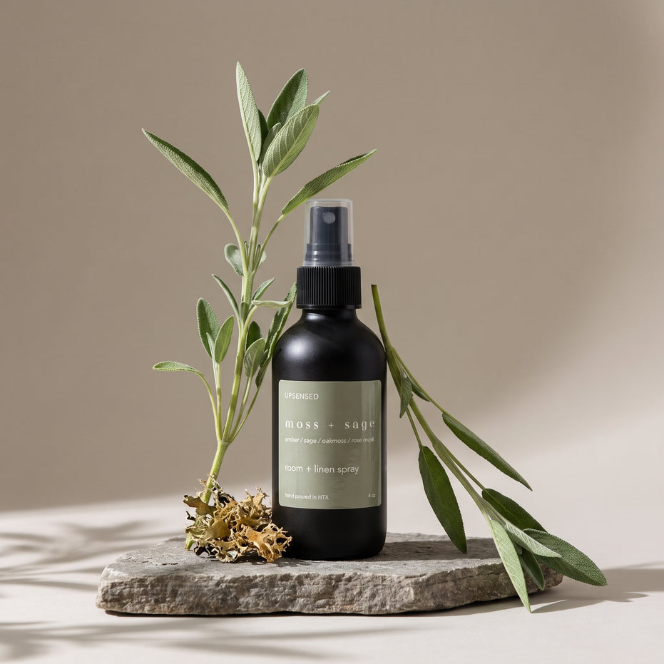 Moss + Sage room and linen spray on a stone slab with fresh sage stems and dried oakmoss.