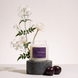 Upsensed Nocturne candle burning on a dark round stone pedestal, styled with white night-blooming jasmine and epiphyllum flowers and two dark plums.