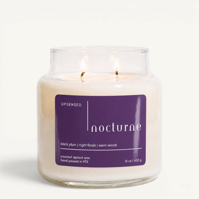Upsensed Nocturne 16 oz double-wick candle in a clear apothecary jar with a deep purple label, black plum, night florals, and warm woods scent notes, on a plain white background.