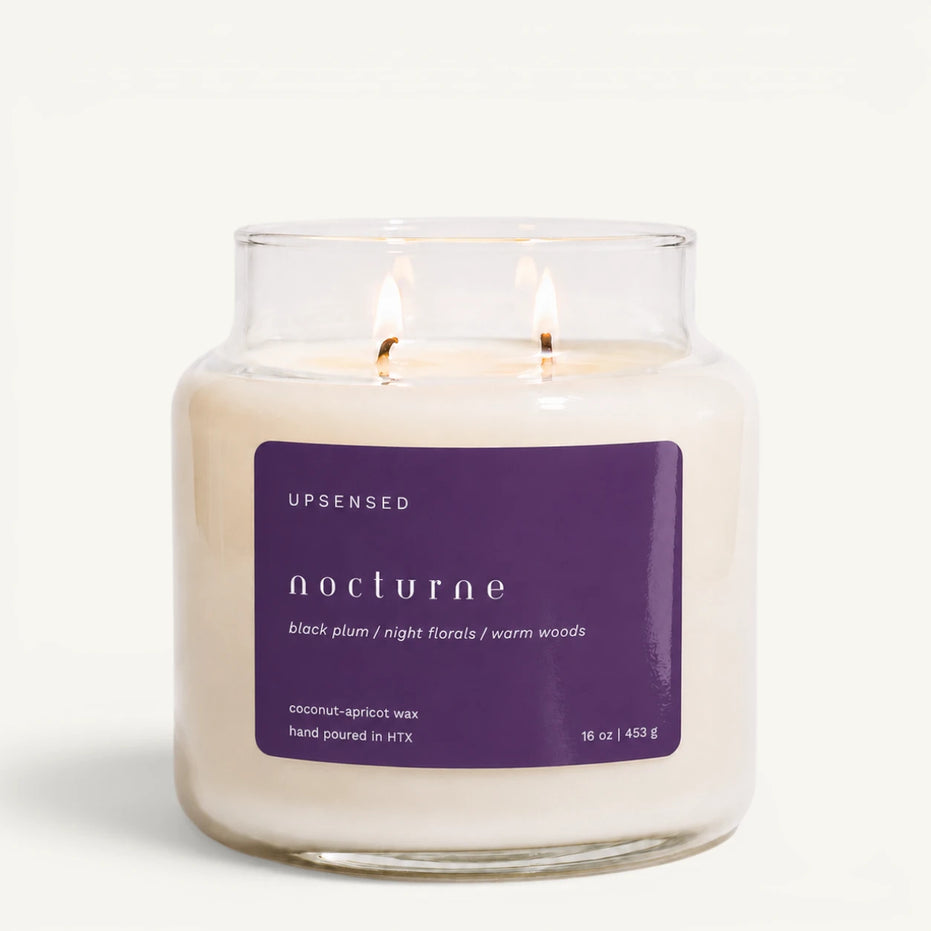 Upsensed Nocturne 16 oz double-wick candle in a clear apothecary jar with a deep purple label, black plum, night florals, and warm woods scent notes, on a plain white background.
