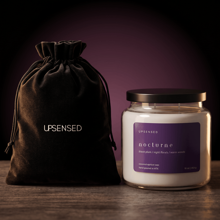 Upsensed Nocturne candle with a black lid beside its black velvet UPSENSED drawstring packaging bag, on a dark moody purple background.