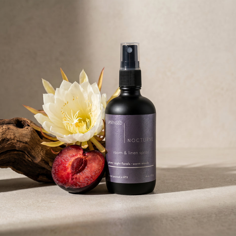 Upsensed Nocturne Room and Linen Spray beside sliced plum night blooming flower and driftwood - dark floral home fragrance hand poured in Houston