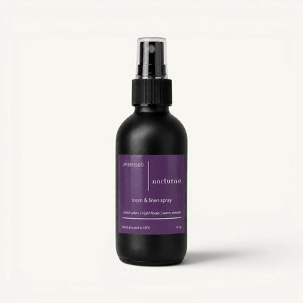 Upsensed Nocturne room and linen spray in a matte black 4 oz bottle with a deep purple label, black plum, night florals, and warm woods scent notes, on a plain white background.