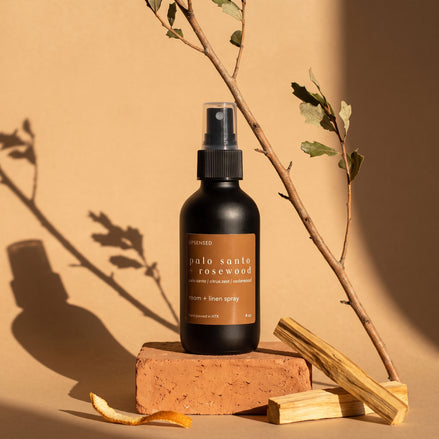 Palo Santo + Rosewood room and linen spray on a terracotta brick with palo santo sticks and dried citrus peel.