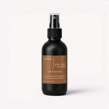 Upsensed Palo Santo + Rosewood room and linen spray in a matte black 4 oz bottle with a tan label, palo santo, citrus zest, and cedarwood scent notes, on a plain white background.