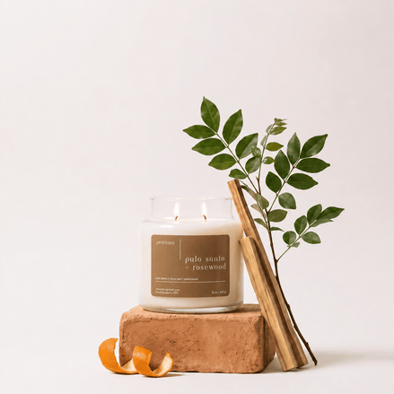 Upsensed Palo Santo + Rosewood candle burning on a terracotta brick, styled with a leafy branch, palo santo sticks, and a curled orange peel against a neutral background.