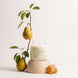 Upsensed Pearfect candle burning on a light wood pedestal, styled with a pear branch and a piece of honeycomb.