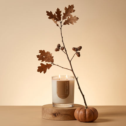 Lit Upsensed Pumpkin + Oak candle on a round oak slab with an autumn oak branch, acorns, and a small orange pumpkin