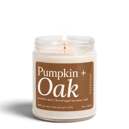 Upsensed Pumpkin + Oak 8 oz soy candle, lit, in a clear glass jar with a caramel brown label listing pumpkin spice, barrel-aged bourbon, and oak