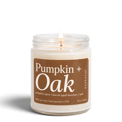 Upsensed Pumpkin + Oak 8 oz soy candle, lit, in a clear glass jar with a caramel brown label listing pumpkin spice, barrel-aged bourbon, and oak
