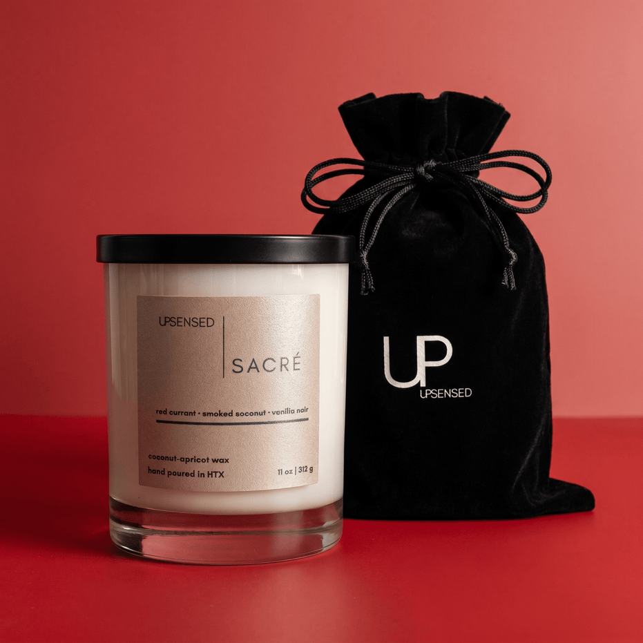 Upsensed Sacré candle beside reusable black velvet drawstring gift bag on rich red background