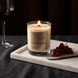 Upsensed Sacré candle burning on a marble tray beside fresh red currants, a vanilla bean, and a glass of red wine against a dark moody background