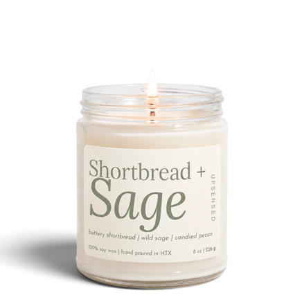Upsensed Shortbread + Sage 8 oz soy candle, lit, in a clear glass jar with a cream label and sage green lettering listing buttery shortbread, wild sage, and candied pecan