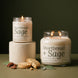 Shortbread + Sage soy candle in two sizes: a lit 8 oz single-wick jar on a cream plaster pedestal beside a lit 18 oz double-wick jar, both with cream labels, with shortbread cookies, candied pecans, and sage leaves against an olive green background