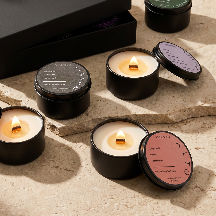 Upsensed Candle Discovery Set — multiple 2 oz mini candles with wood wicks burning in matte black tins displayed on a stone surface with black gift box, including Alto, Lignum, Quietude, and Higher Ground fragrances from the Signature Collection, hand poured in Houston with coconut-apricot wax