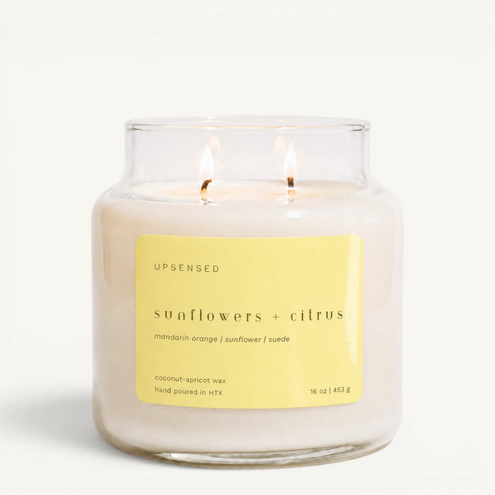 Upsensed Sunflowers + Citrus 16 oz double-wick candle in a clear apothecary jar with a yellow label, mandarin orange, sunflower, and suede scent notes, on a plain white background.