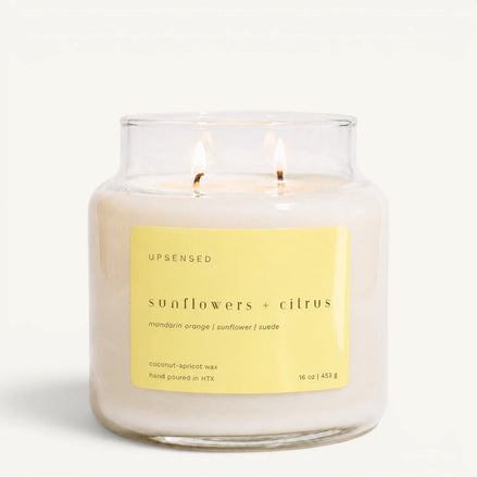 Upsensed Sunflowers + Citrus 16 oz double-wick candle in a clear apothecary jar with a yellow label, mandarin orange, sunflower, and suede scent notes, on a plain white background.