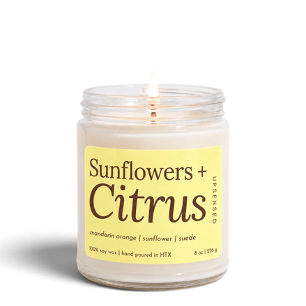 Upsensed Sunflowers + Citrus 8 oz soy candle, lit, in a clear glass jar with a butter yellow label listing mandarin orange, sunflower, and suede