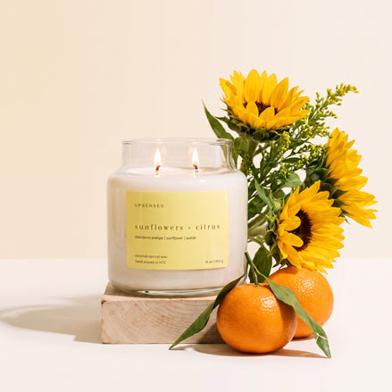 Upsensed Sunflowers + Citrus candle on a light wood block, styled with fresh sunflowers and mandarin oranges against a cream background.