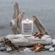 Upsensed Undertow candle burning on a large driftwood log at the coast, surrounded by sea salt, cedar wood chips, and smooth river stones