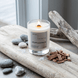 Upsensed Undertow coastal candle burning on weathered driftwood surrounded by sea salt, smooth stones, and cedar chips