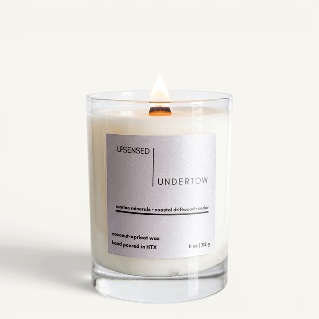 Upsensed Undertow candle lit on white background, showing silver-grey label with marine minerals, coastal driftwood, and cedar notes