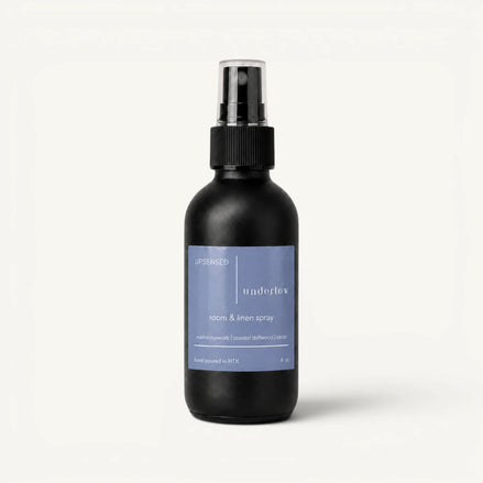Upsensed Undertow room and linen spray in a matte black 4 oz bottle with a dusty blue label, marine minerals, coastal driftwood, and cedar scent notes, on a plain white background.