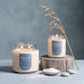 Upsensed Undertow candle in 18 oz double-wick and 8 oz single-wick sizes, lit beside a dish of sea salt and smooth beach stones