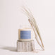 Upsensed Undertow candle burning on a weathered wood block, styled with a piece of driftwood, dried coastal grass, and scattered sea salt.