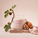 Upsensed Intention candle burning on a pink marble slab, styled with a fig branch, a halved fig, a pear, and draped pink silk fabric.