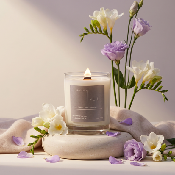 Upsensed Veil 11oz scented candle burning with wood wick surrounded by white freesia and violet flowers on soft cashmere fabric - coconut apricot wax candle hand poured in Houston