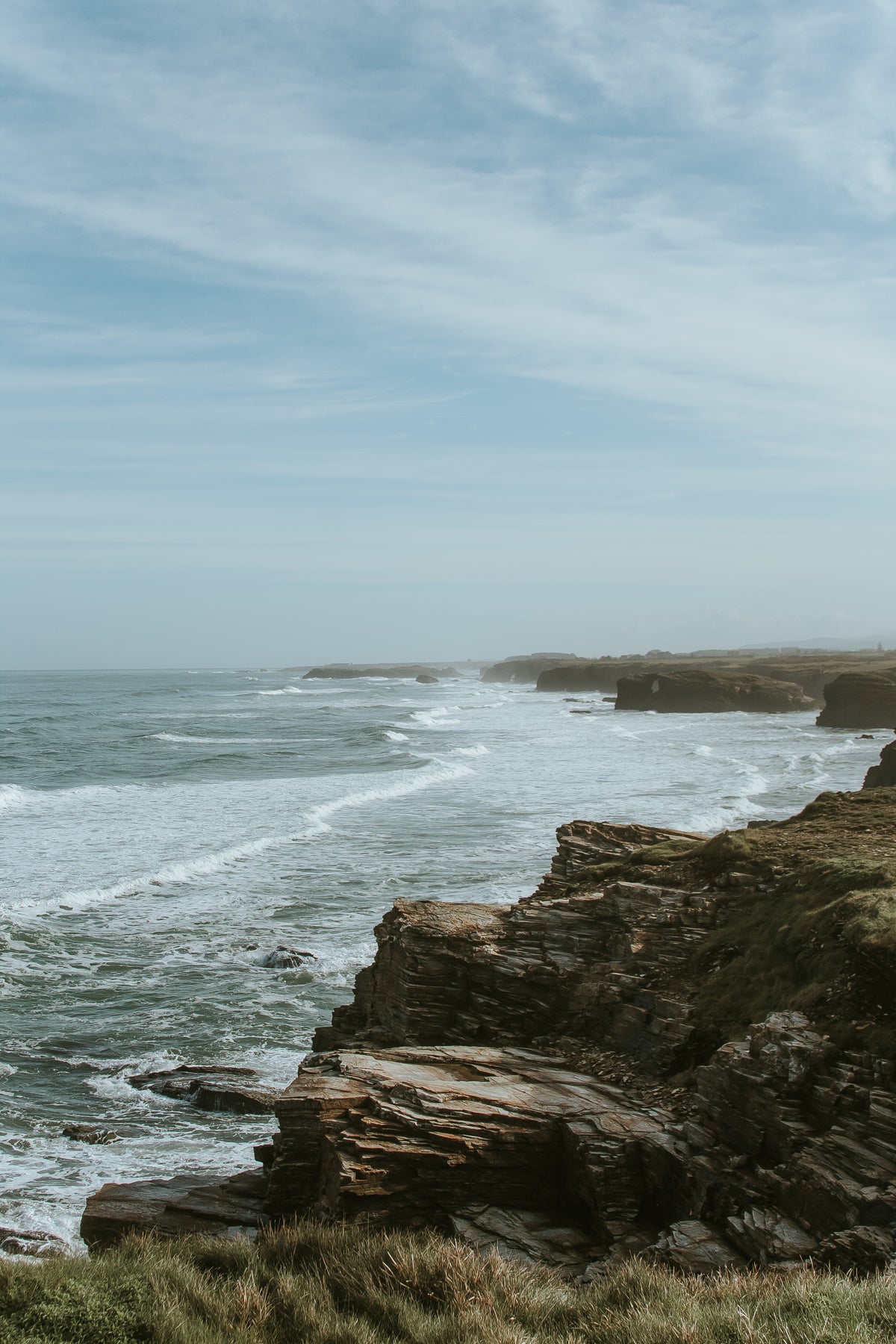 Rugged coastal cliffside with crashing ocean waves under an overcast sky — editorial background image for Upsensed Undertow candle, a marine mineral and driftwood scented candle hand-poured in Houston