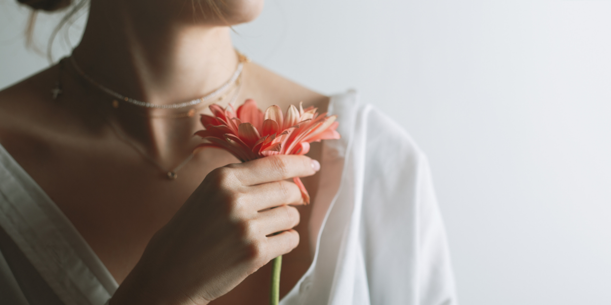 Person holding a pink flower against a neutral background